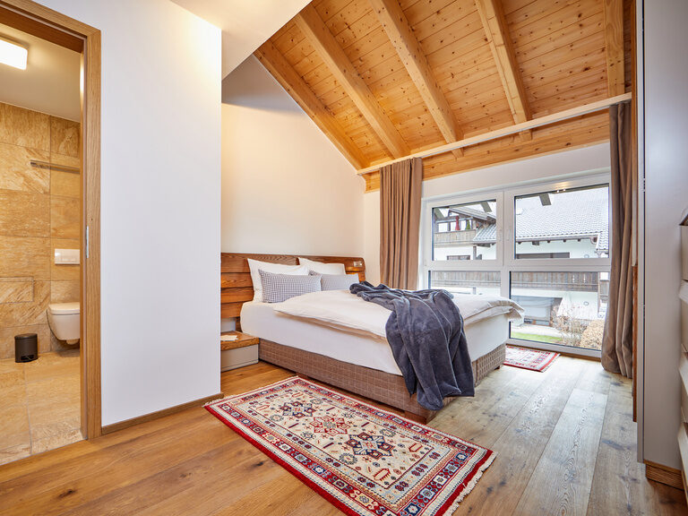 Großes Schlaf- und Badezimmer mit edlem Holzboden und wunderschöner Aussicht durch das große Balkonfenster der Bader Suites.
