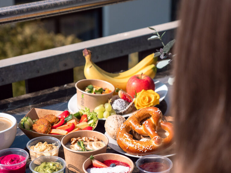 Eine Frau sitzt an einem reich gedeckten Tisch auf dem Balkon eines Apartments der Bader Suites.