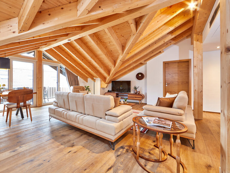 Ein stilvoller Esstisch aus Holz mit bequemen Sitzmöglichkeiten sowie eine einladende Couch mit Fernseher vor einer großzügigen Fensterfront.