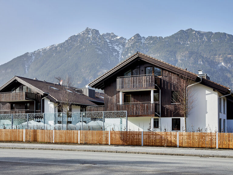 Winterliche Außenansicht zwei Apartmenthäuser der Bader Suites mit atemberaubendem Blick auf die dahinterliegenden Berge in Garmisch-Partenkirchen.