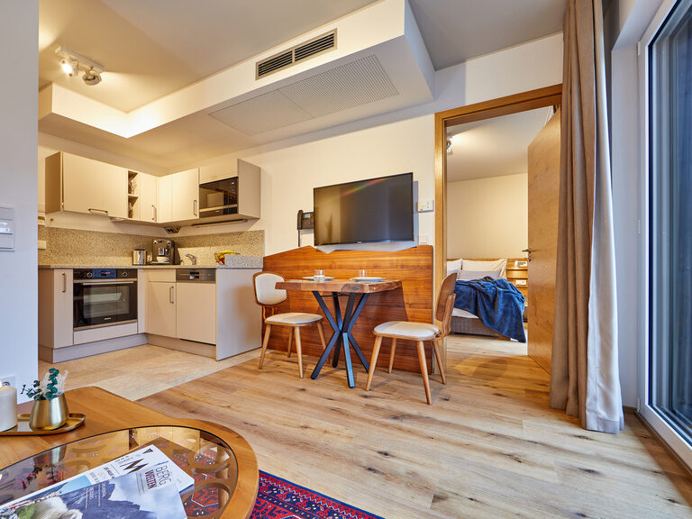 Ein gemütliches Esszimmer mit heller Beleuchtung, passenden Stühlen, einem Holztisch und einer modernen Küche mit Zugang zum Schlafzimmer.