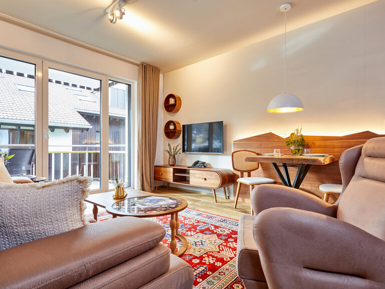 Behagliche Wohneinrichtung mit Flachbildfernseher und Couch im Apartment Superior, mit großzügigem Ausblick durch das weitläufige Balkonfenster.