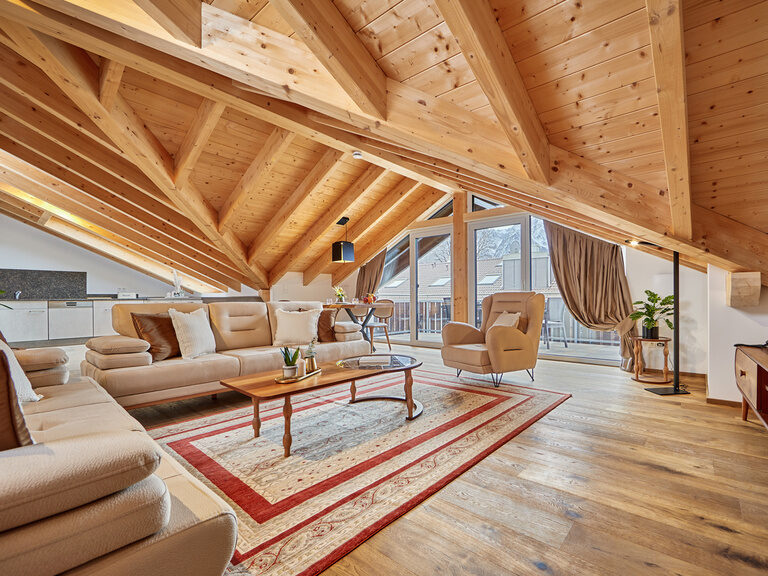 Ein einladendes, großes Apartment mit gemütlicher Coucheinrichtung und Flachbildfernseher, dessen weitläufiges Balkonfenster für viel Lichteinfall sorgt.