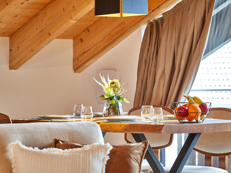 Ein stilvoll gedeckter Holztisch mit moderner Beleuchtung im Apartment der Bader Suites mit Ausblick durch das Balkonfenster.