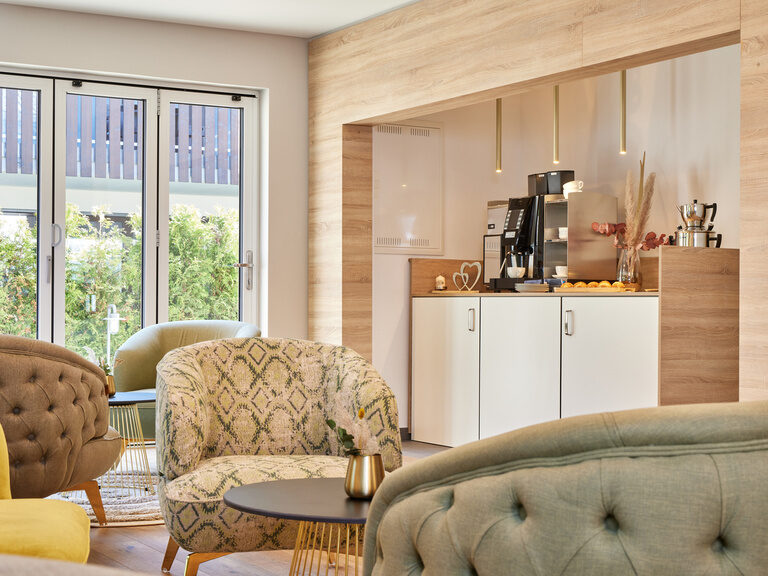 Stilvolles Wohnzimmer in den Bader Suites mit gemütlichen Sofas und eleganten Sesseln vor einer modernen Küche.